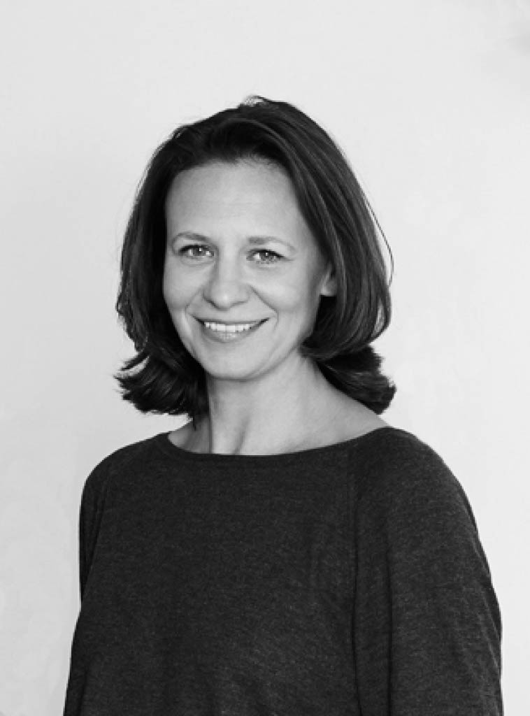 Eine lächelnde Frau mit schulterlangem Haar in einem dunklen Oberteil, vor einem neutralen Hintergrund.