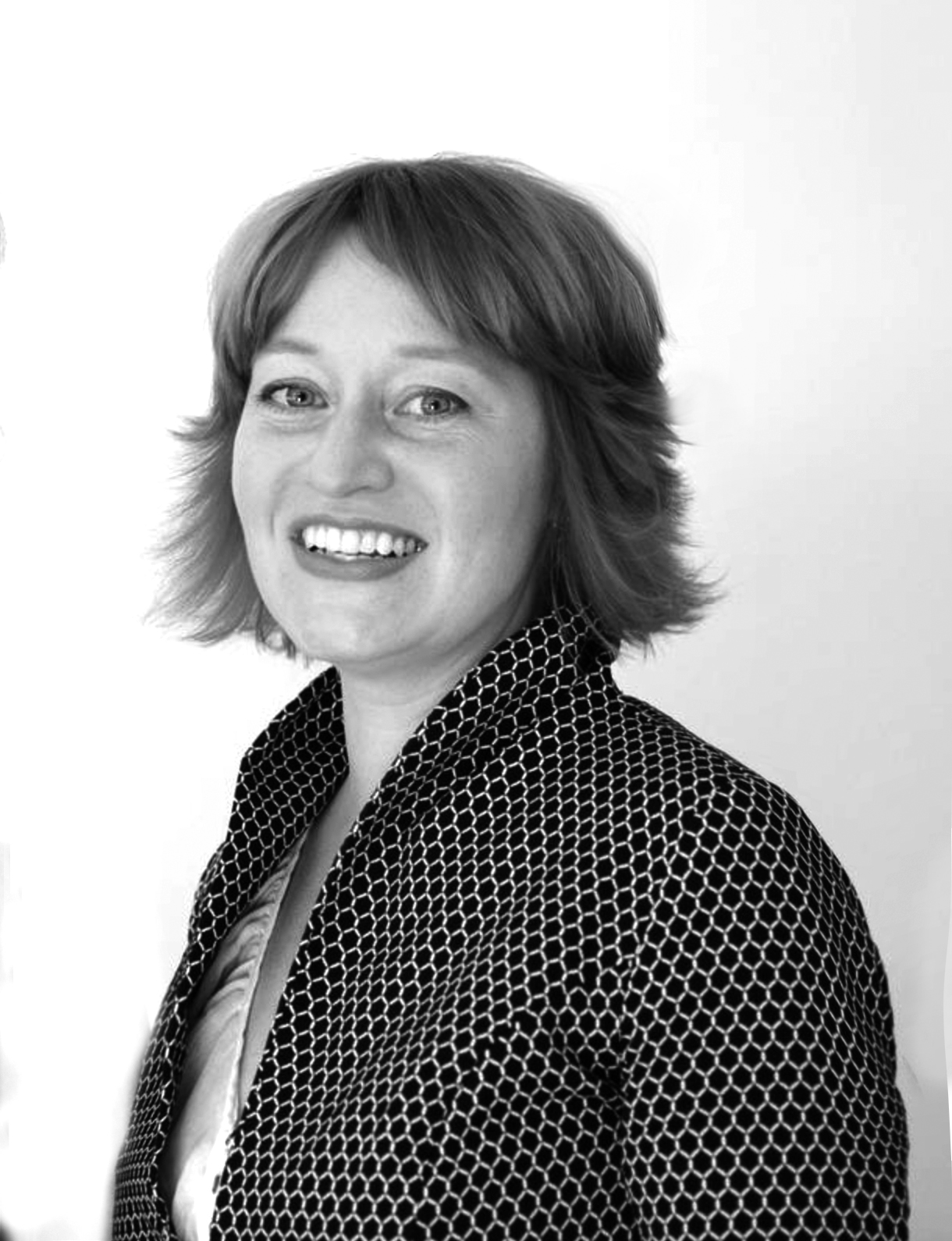 Eine Frau mit lächelndem Gesicht, kurzen Haaren und einem gemusterten schwarzen Blazer.